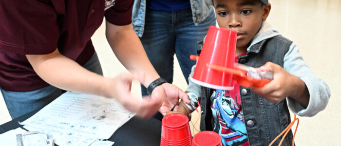 Grayison Tirado, 5, of Princess Anne, gets help from Yuhao Qiang with a robotic hand during the 2025 UMES 4-H STEM Expo.