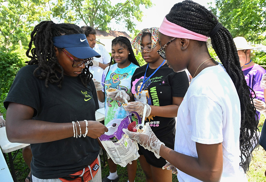 EFNEP intern Bianca Oliver adds fruit to Marly Point-Dujour’s yoghurt bowl as part of a nutrition lesson during a visit to the Todd Family Community Garden in Princess Anne.